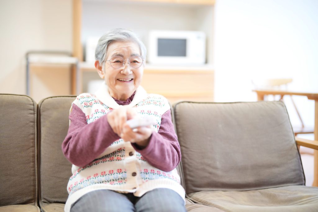 テレビのリモコンを持つ笑顔の高齢女性